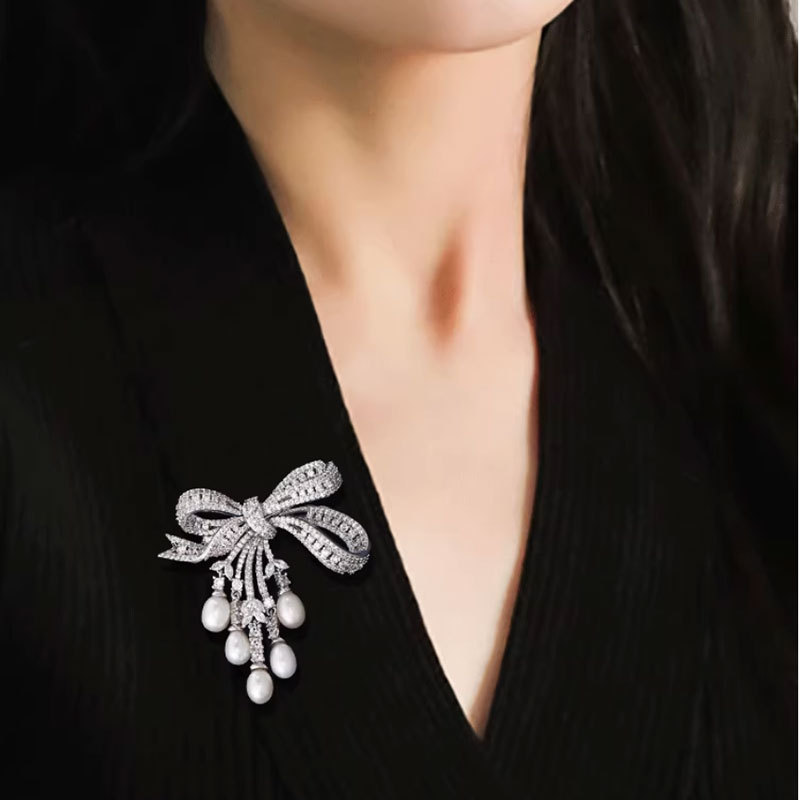 A delicate and luxurious brooch with bow-shaped tassels and a slightly set zirconia embellishment, along with freshwater pearl pins as accessories.