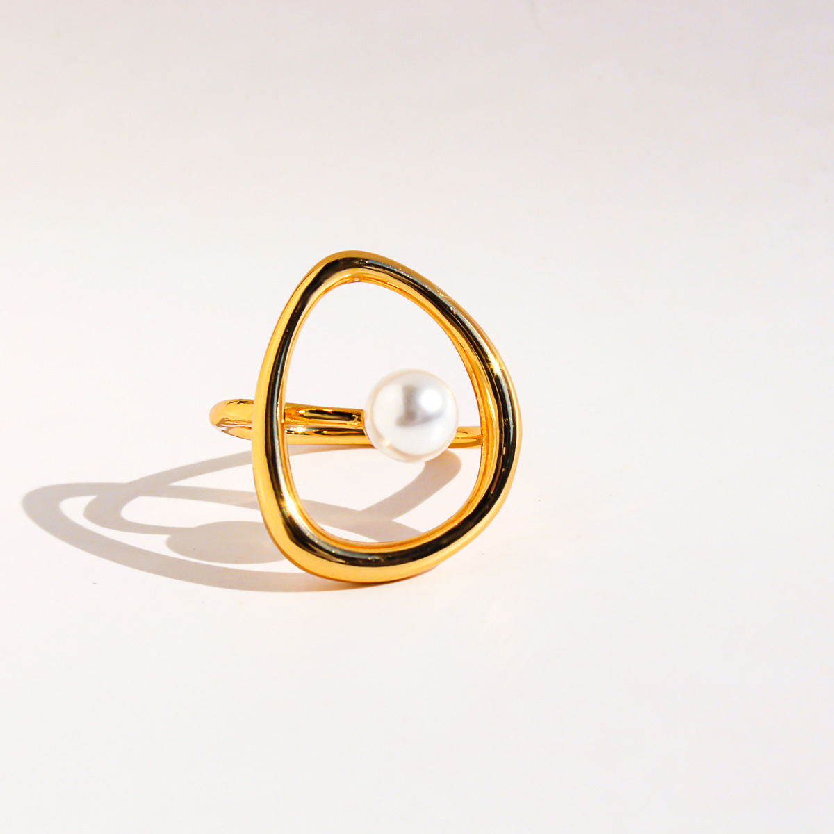 A stylish, abstract pearl ring with a copper-plated, genuine-gold finish and a unique, hollowed-out curved design.