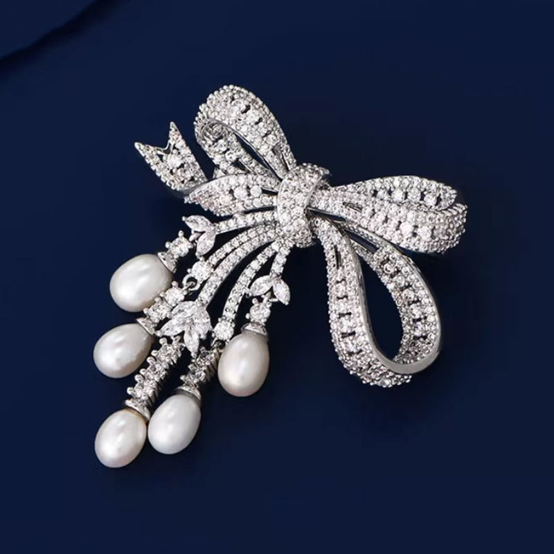 A delicate and luxurious brooch with bow-shaped tassels and a slightly set zirconia embellishment, along with freshwater pearl pins as accessories.